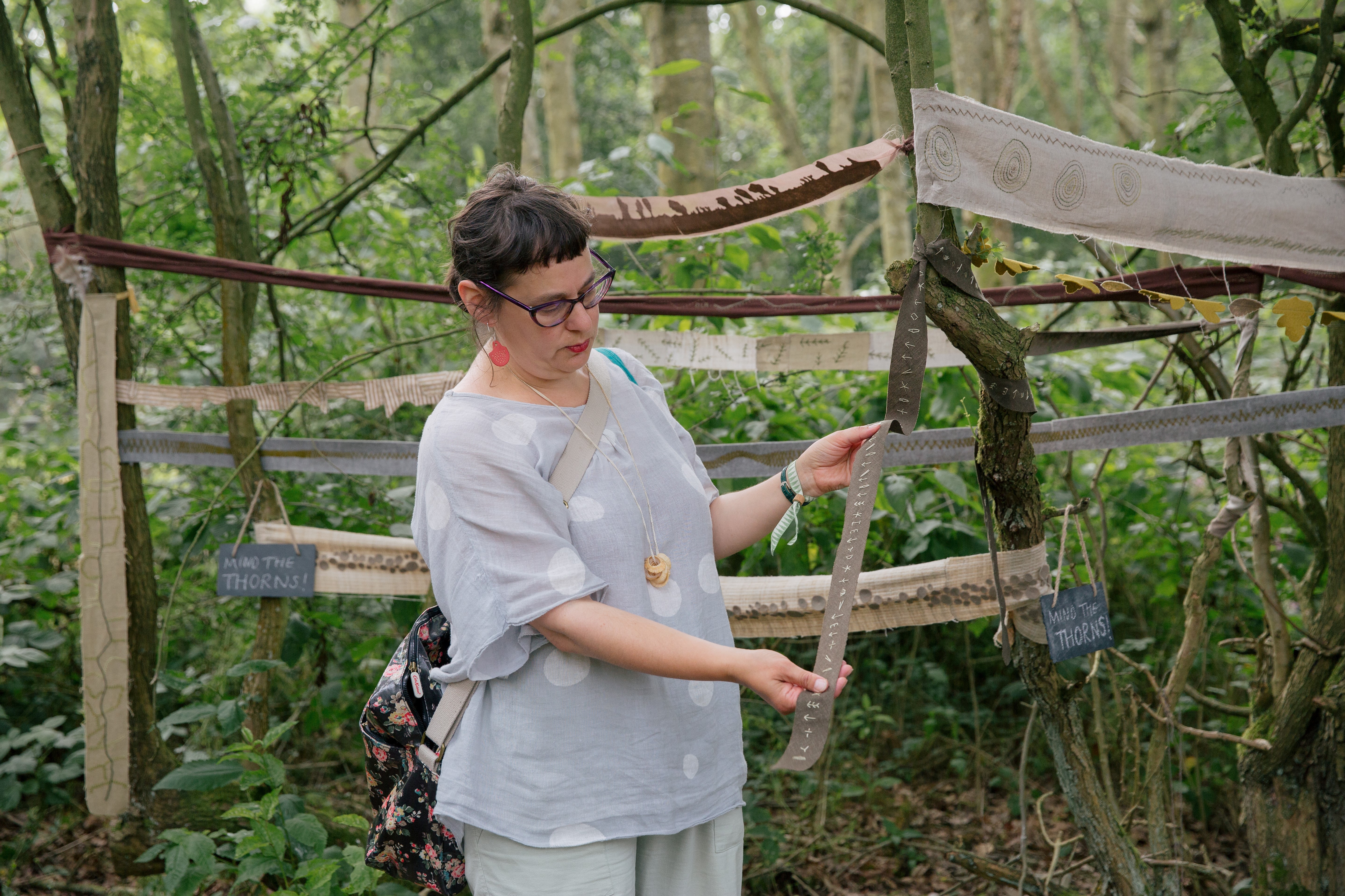 A woman looks at a part of a textile artwork display in a woodland setting