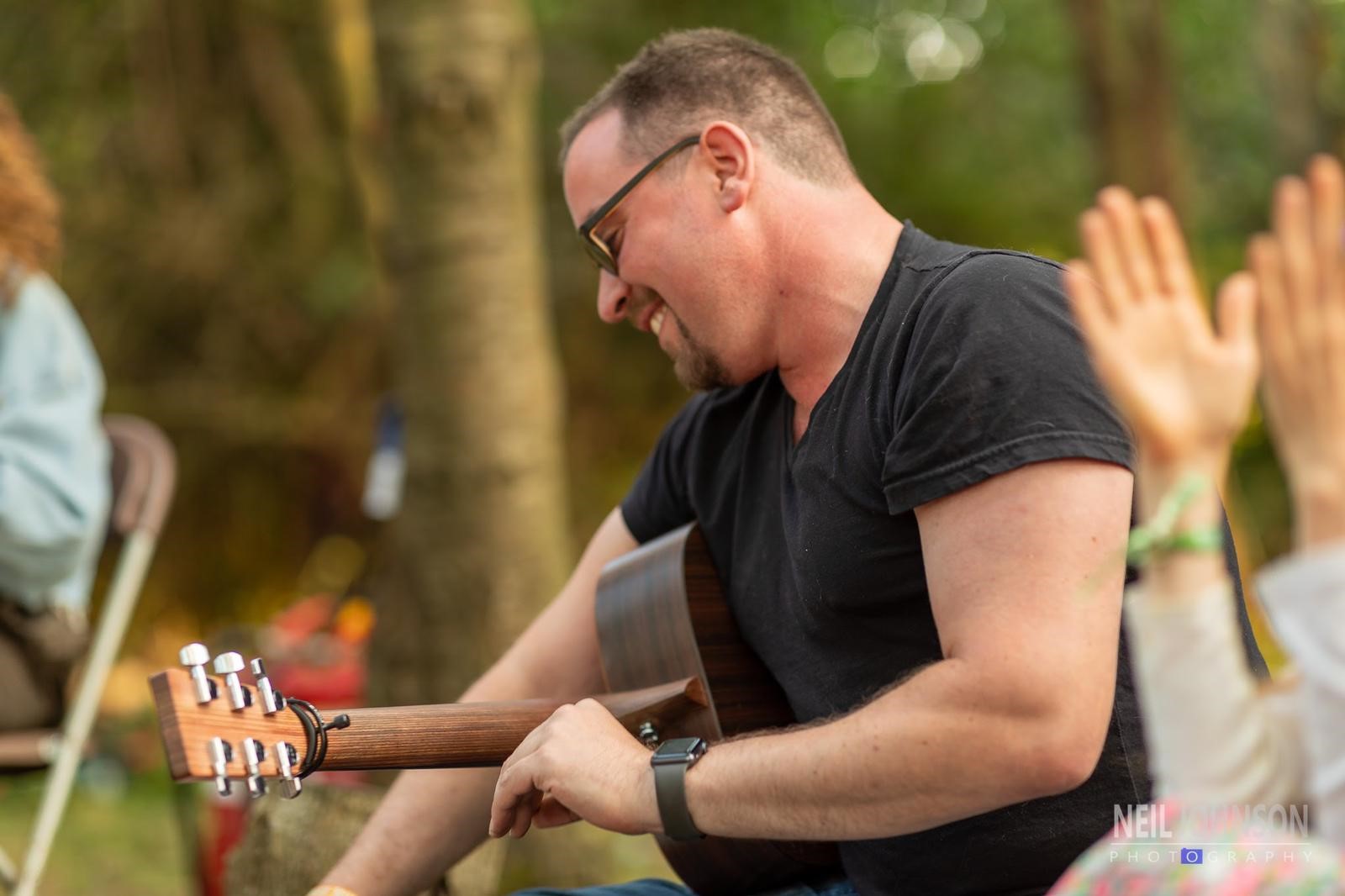 A man smiling as he plays guitar