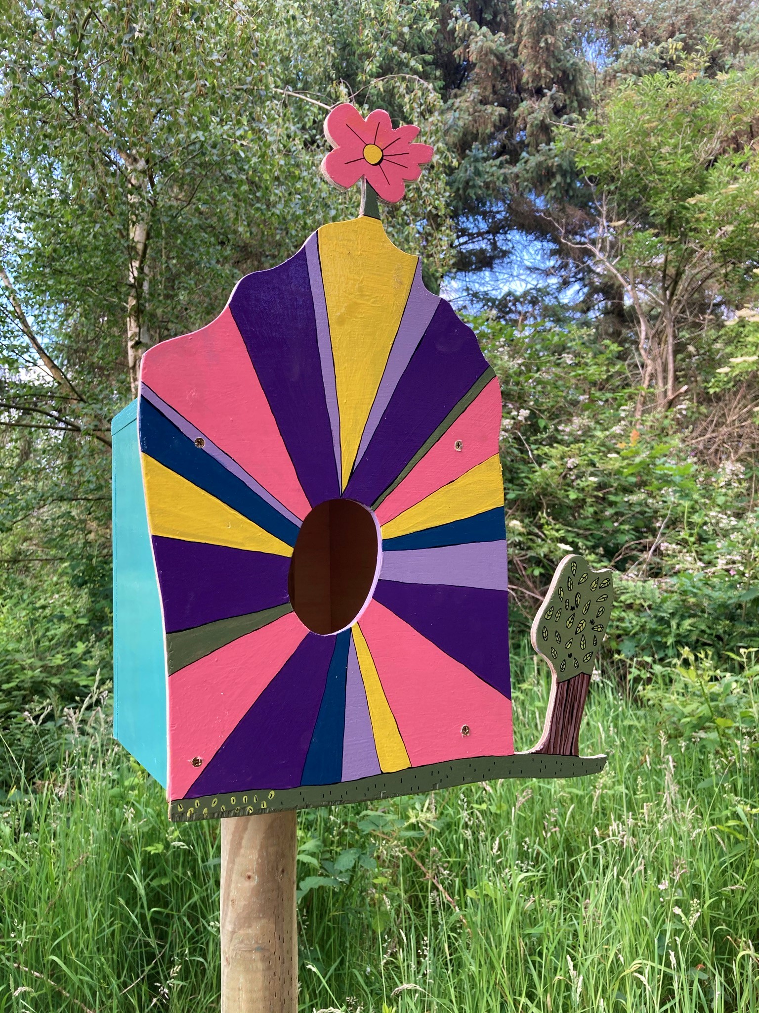 A bird box painted in bright pinks, purples, yellows and blues.