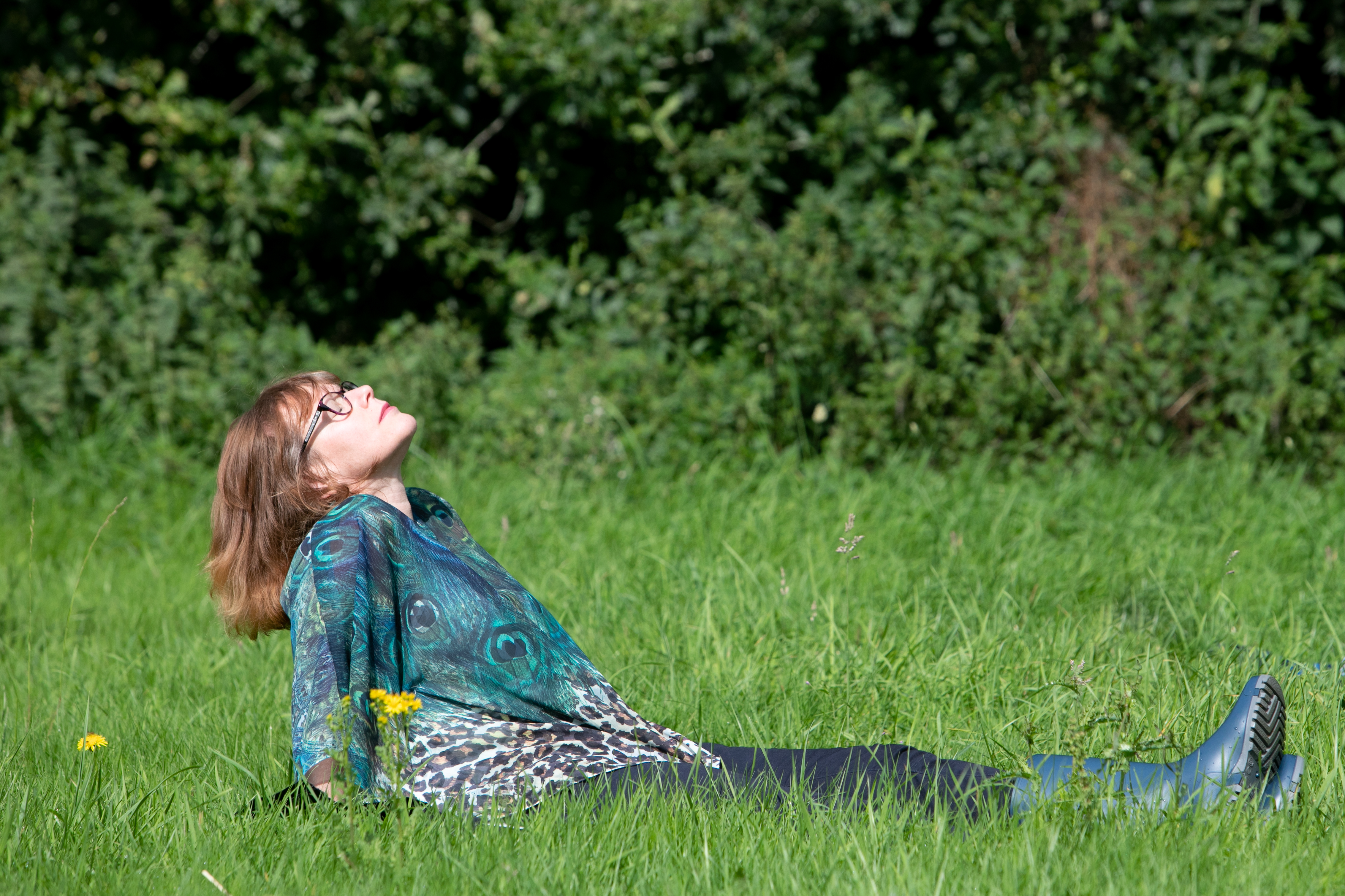 A person sitting in grass, leaning back and looking at the sky with their head tilted up and eyes closed.