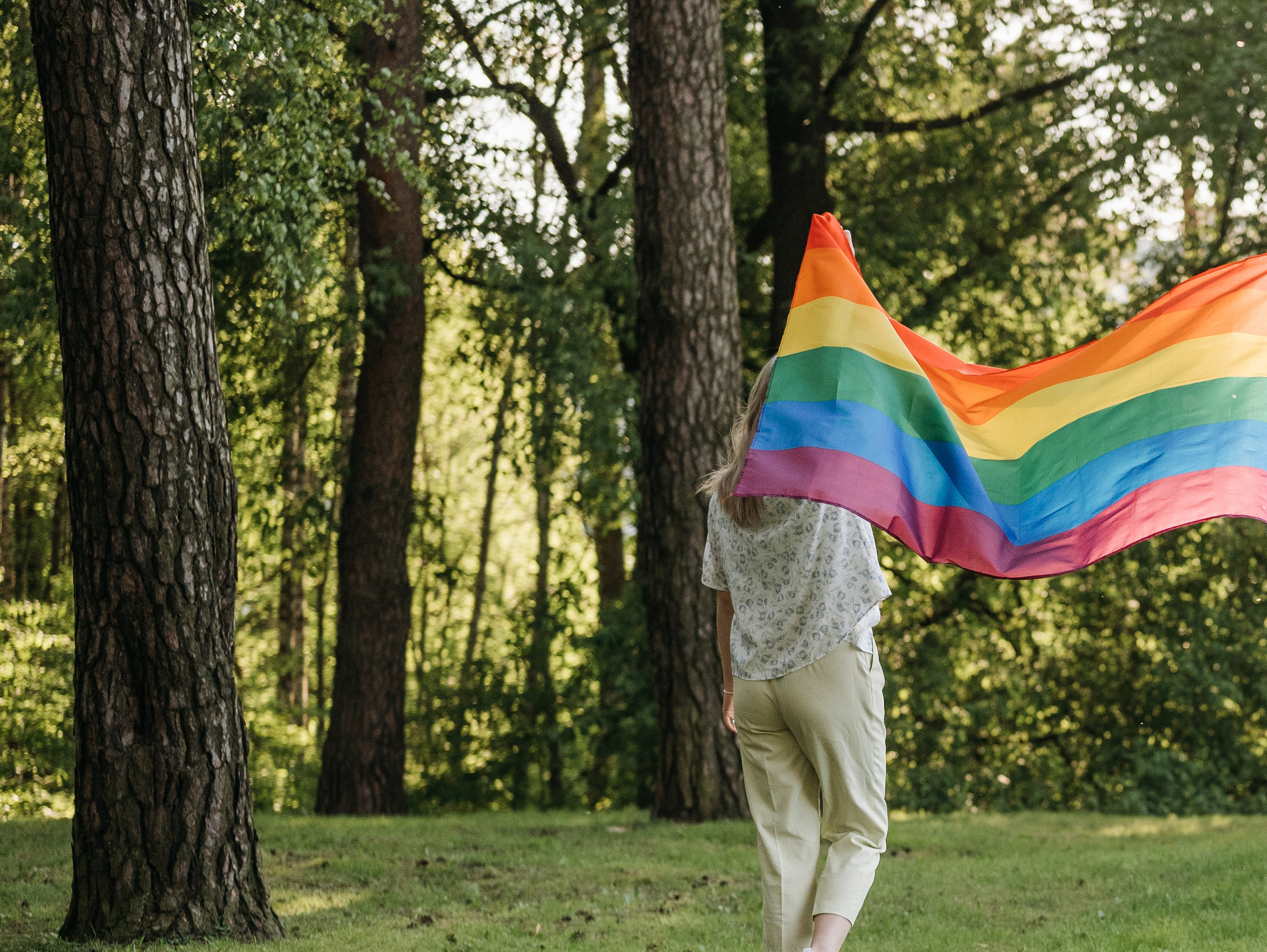 A person holding a pride flag in a woodland